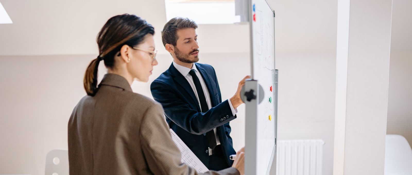Dois profissionais diante de um quadro branco, organizando as etapas de um diagnóstico empresarial